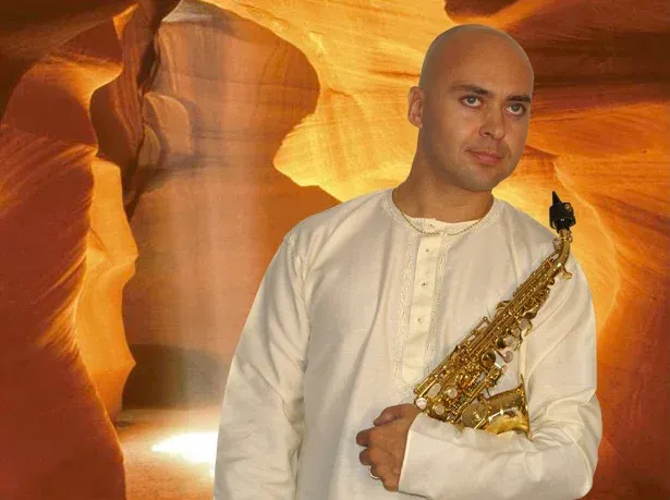 Adrian Sanso-Ali in white, holding his saxophone in a sunlit slot canyon