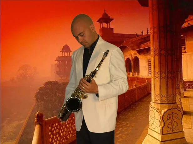 Adrian Sanso-Ali in a white blazer with his saxophone at an Indian palace at sunset